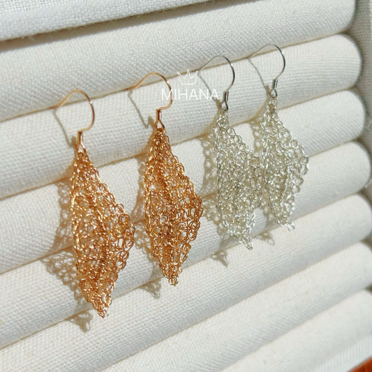 Pair of gold and silver leaf-shaped earrings on a white textured background with 'MIHANA' branding.