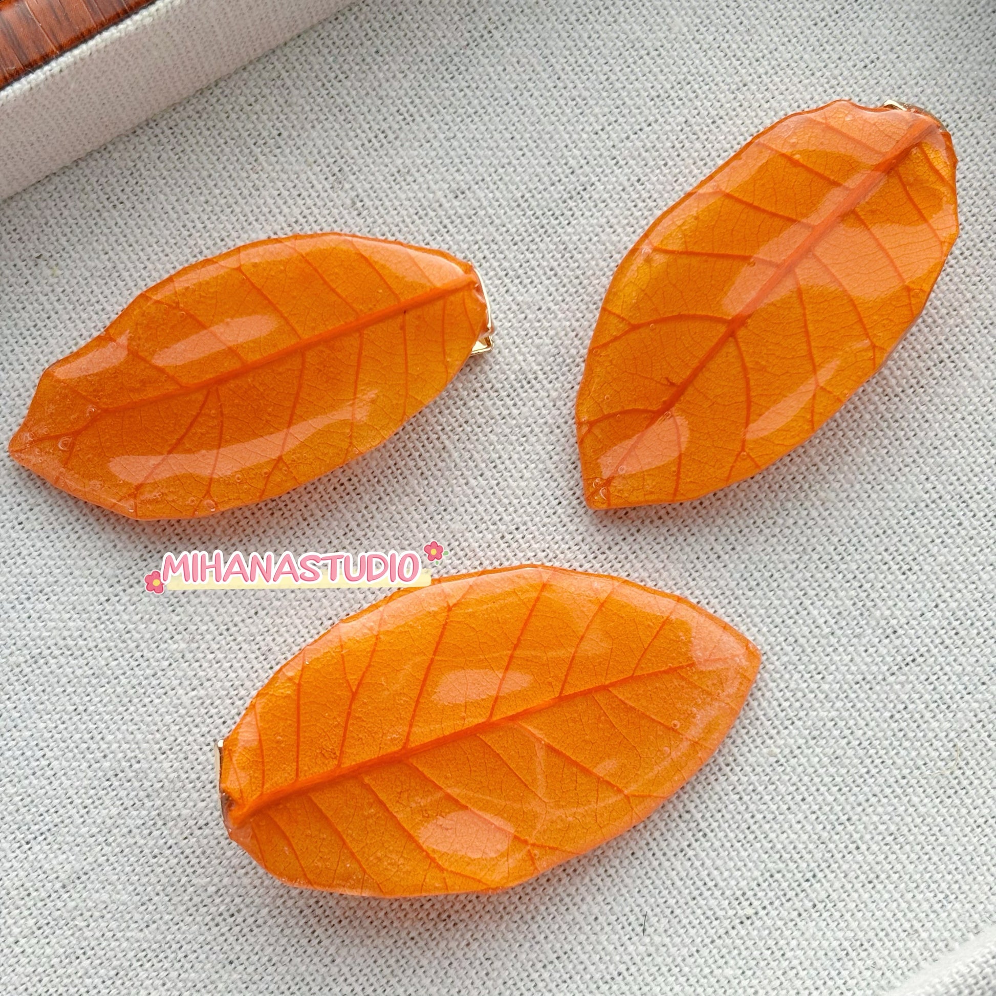 Three orange leaf-shaped objects on a textured gray surface with 'MIHANSTUDIO' branding.