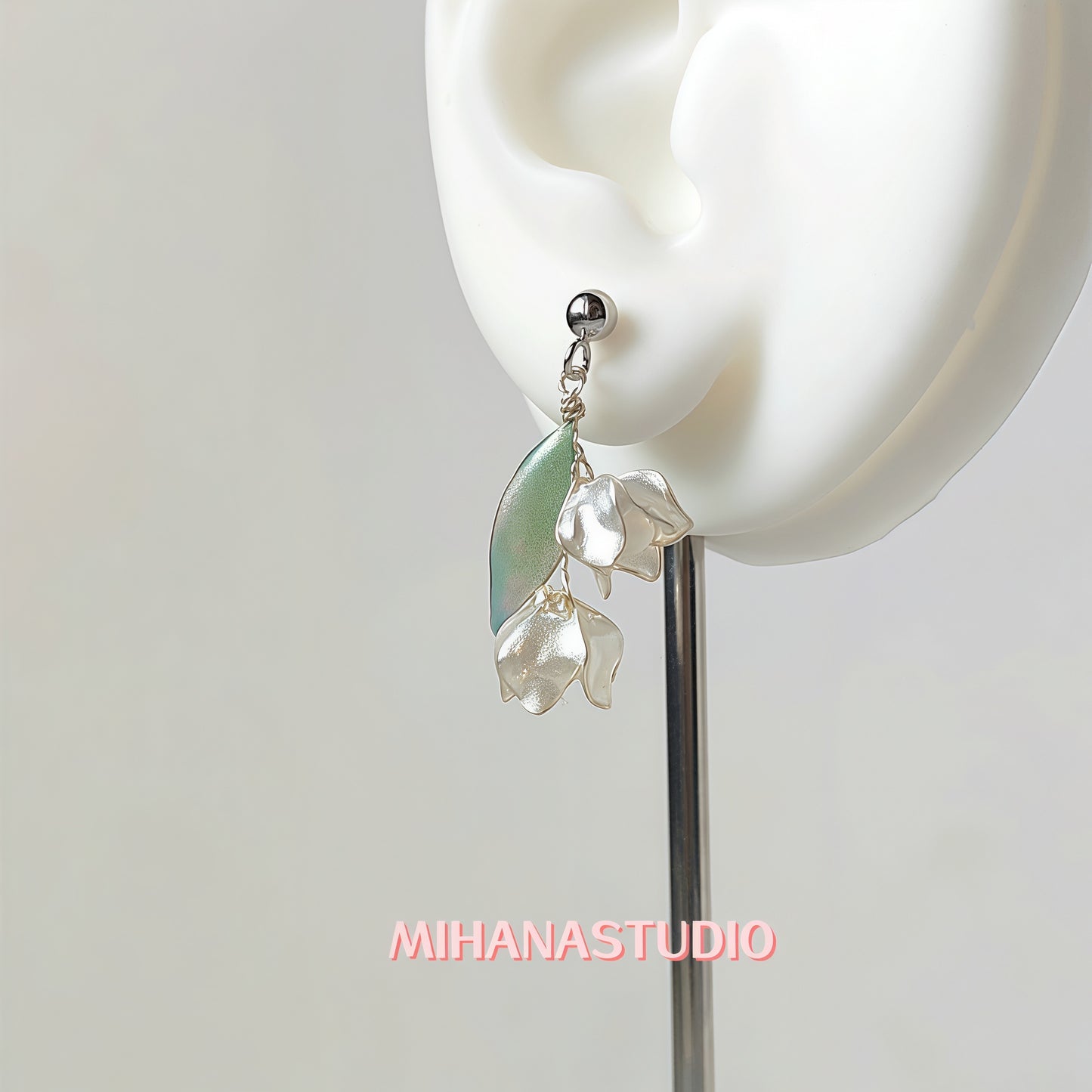 Earring with green and clear elements worn on an ear, brand 'MIHANASTUDIO' visible.