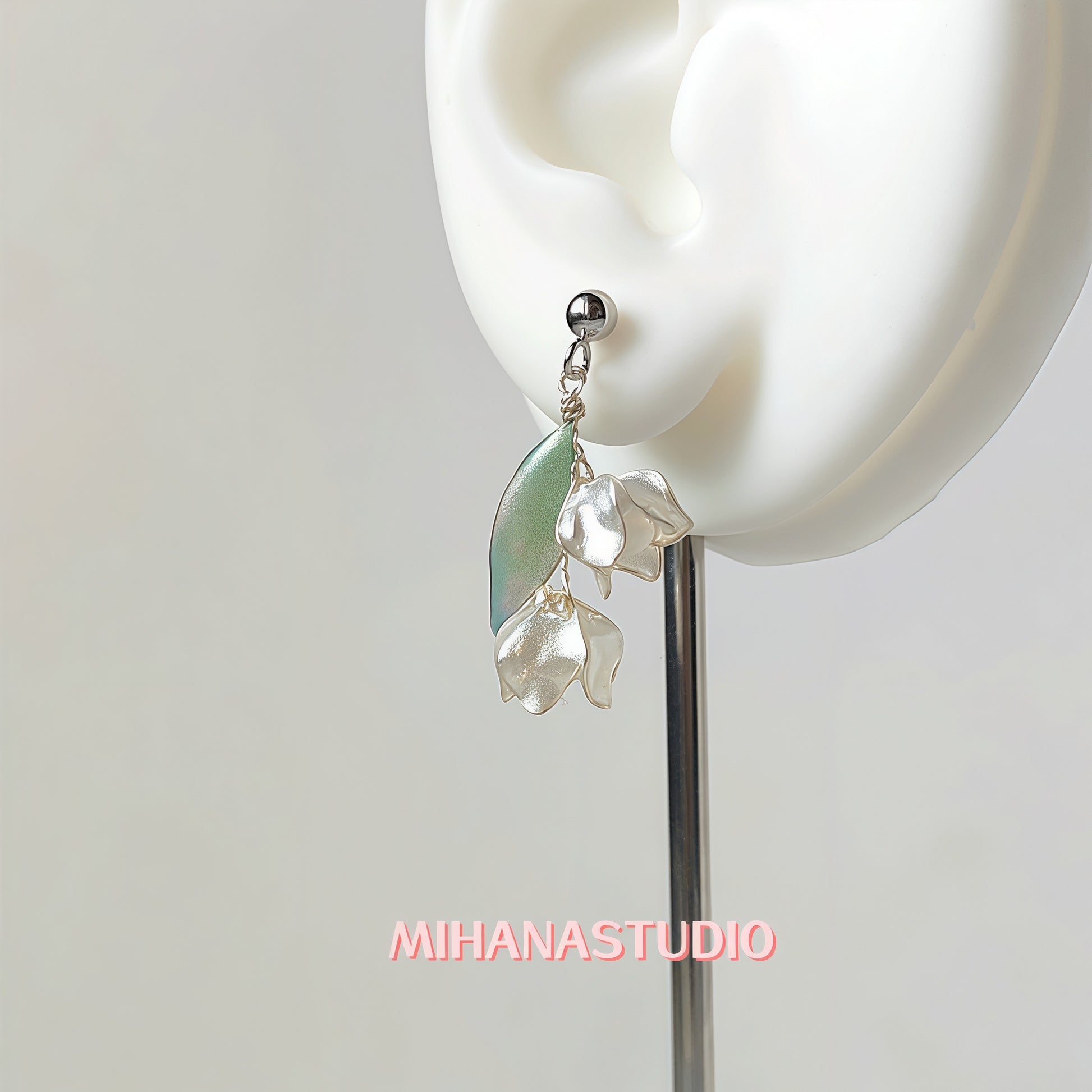 Earring with green and clear elements worn on an ear, brand 'MIHANASTUDIO' visible.
