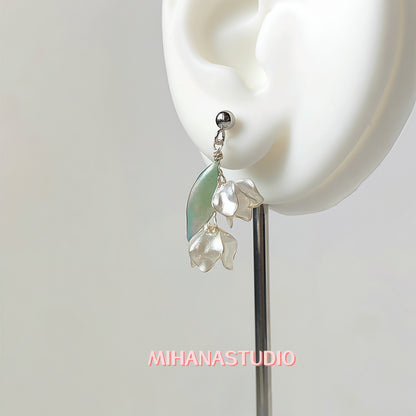 Earring with green and clear elements worn on an ear, brand 'MIHANASTUDIO' visible.