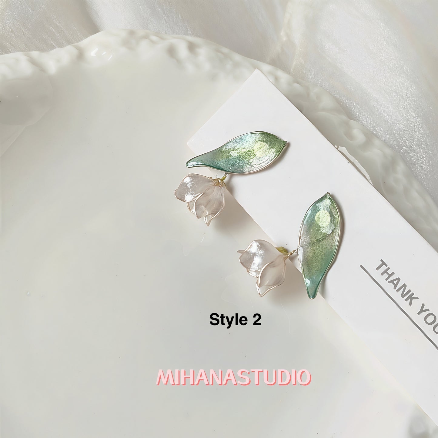 Pair of earrings with leaf and flower design on a white surface, branded 'MIHANASTUDIO'.