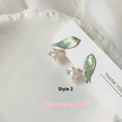 Pair of earrings with leaf and flower design on a white surface, branded 'MIHANASTUDIO'.