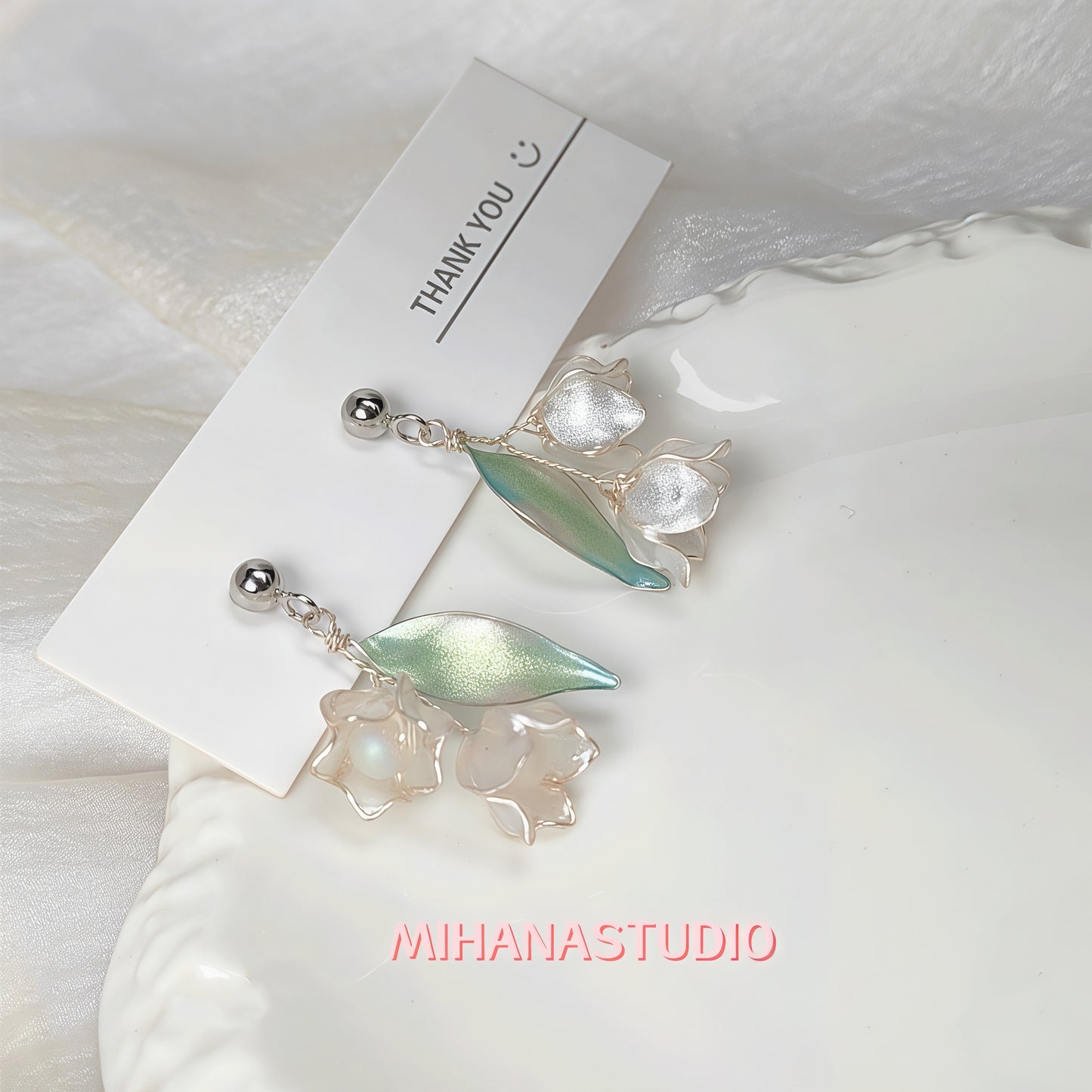 Pair of earrings with leaf-like designs on a white background with 'MIHANASTUDIO' branding.