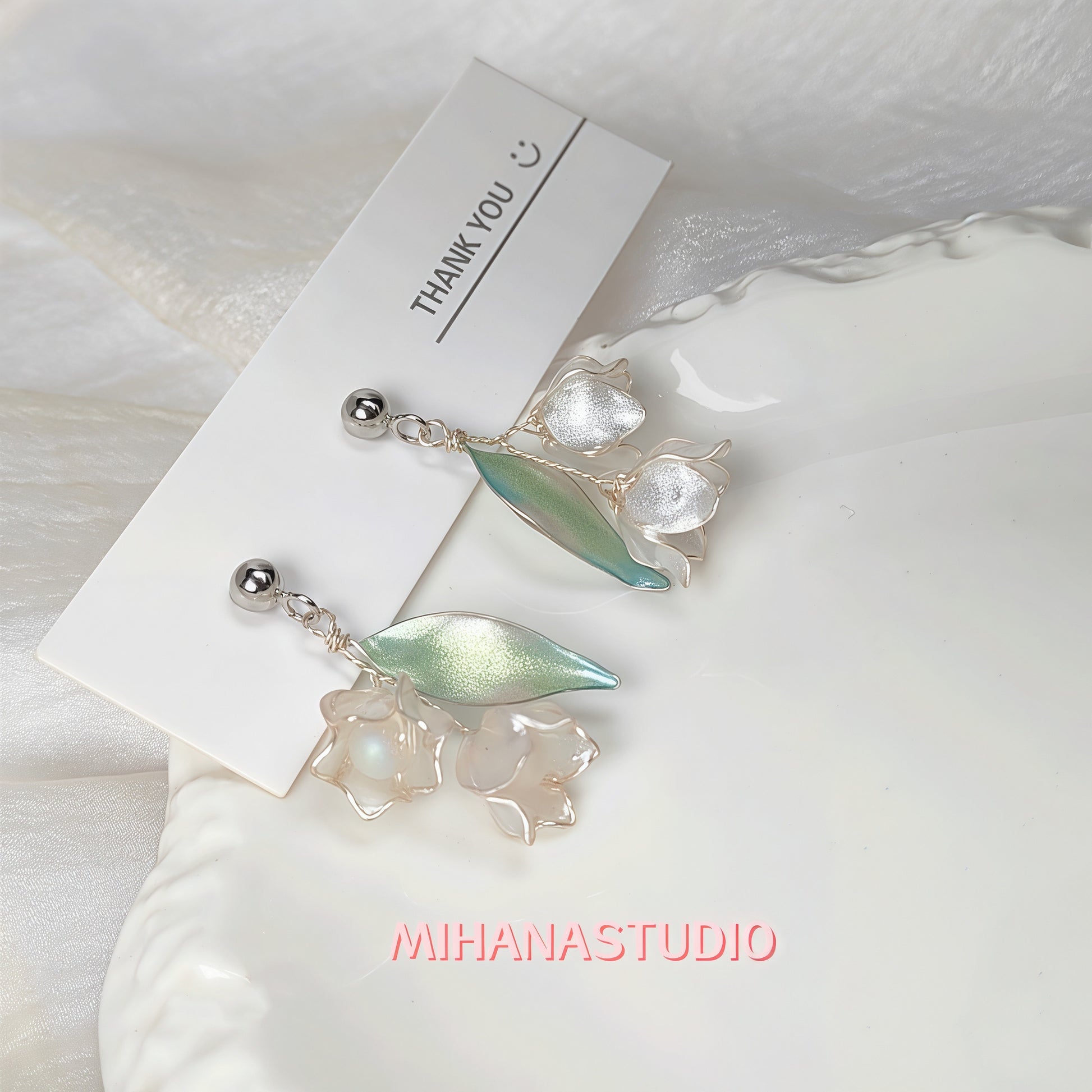 Pair of earrings with leaf-like designs on a white background with 'MIHANASTUDIO' branding.