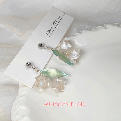 Pair of earrings with leaf-like designs on a white background with 'MIHANASTUDIO' branding.
