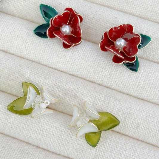 Pair of red flower earrings with green leaves on a white fabric background