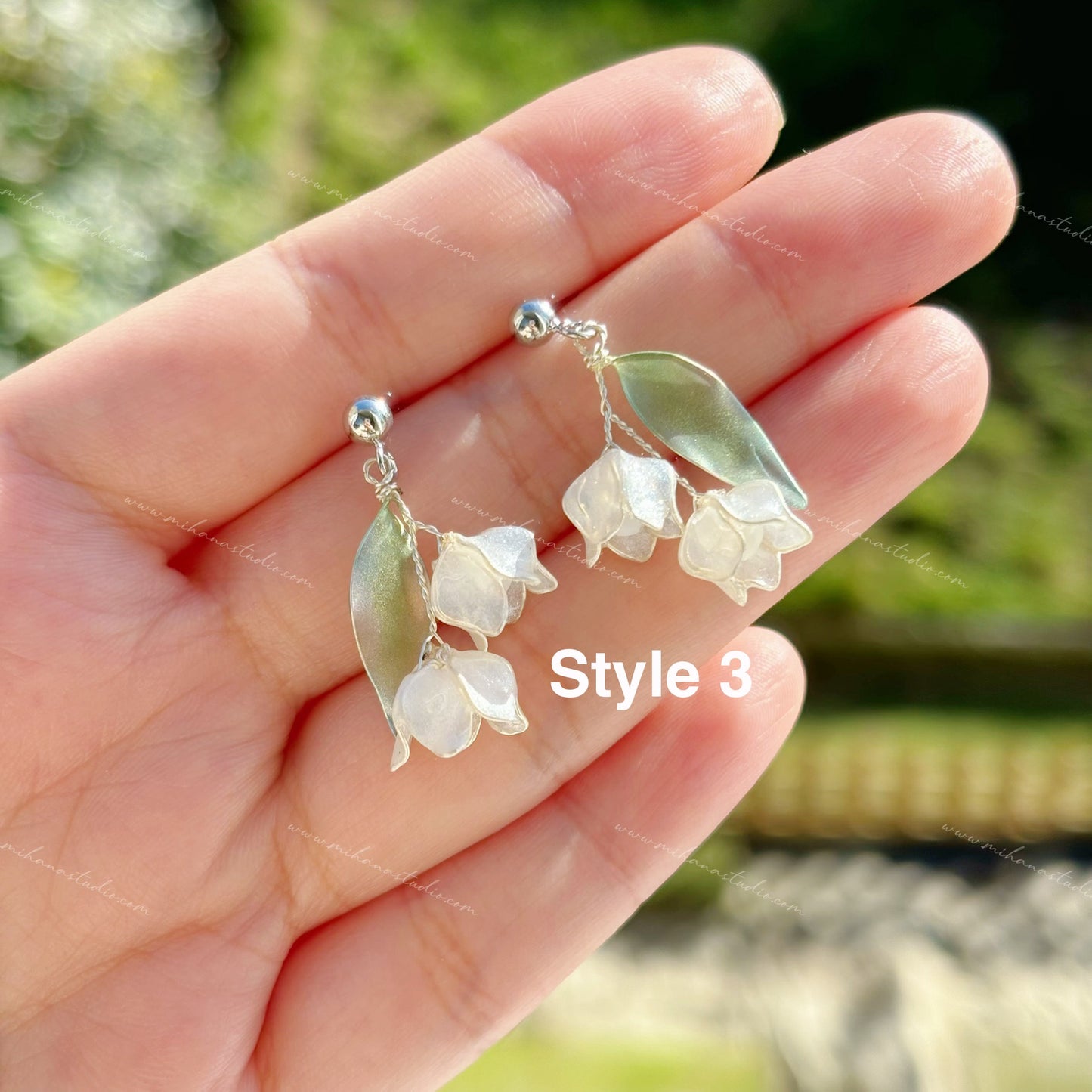 Floral lily of the valley earrings held in a hand with a blurred natural background