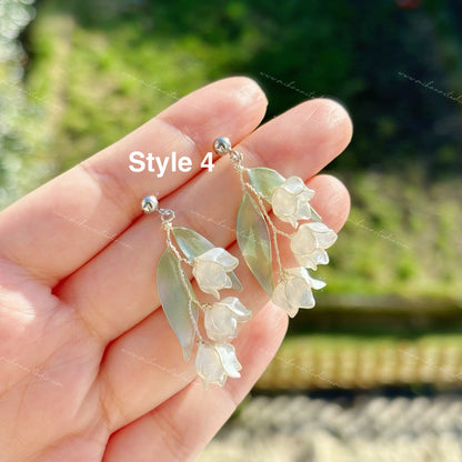 Floral lily of the valley earrings held in a hand with a blurred natural background