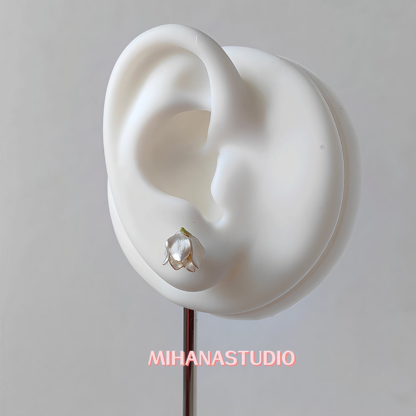 Floral white lily of the valley earring on a mannequin ear with 'MIHANASTUDIO' branding.