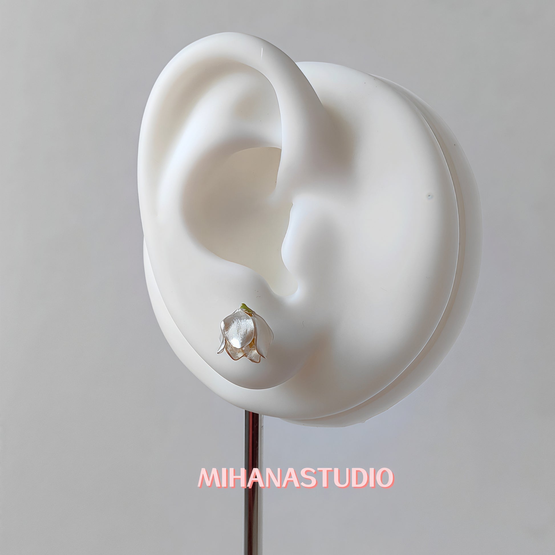 Floral white lily of the valley earring on a mannequin ear with 'MIHANASTUDIO' branding.