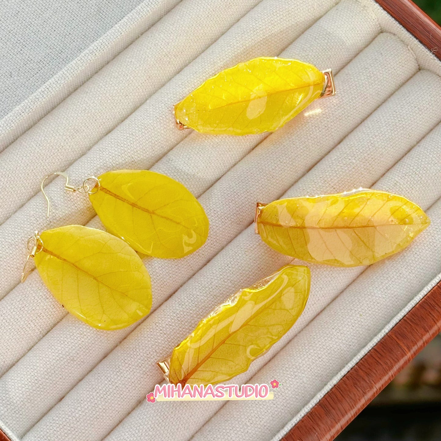 Yellow leaf-shaped earrings on a jewelry display box with 'MIHANA STUDIO' branding.