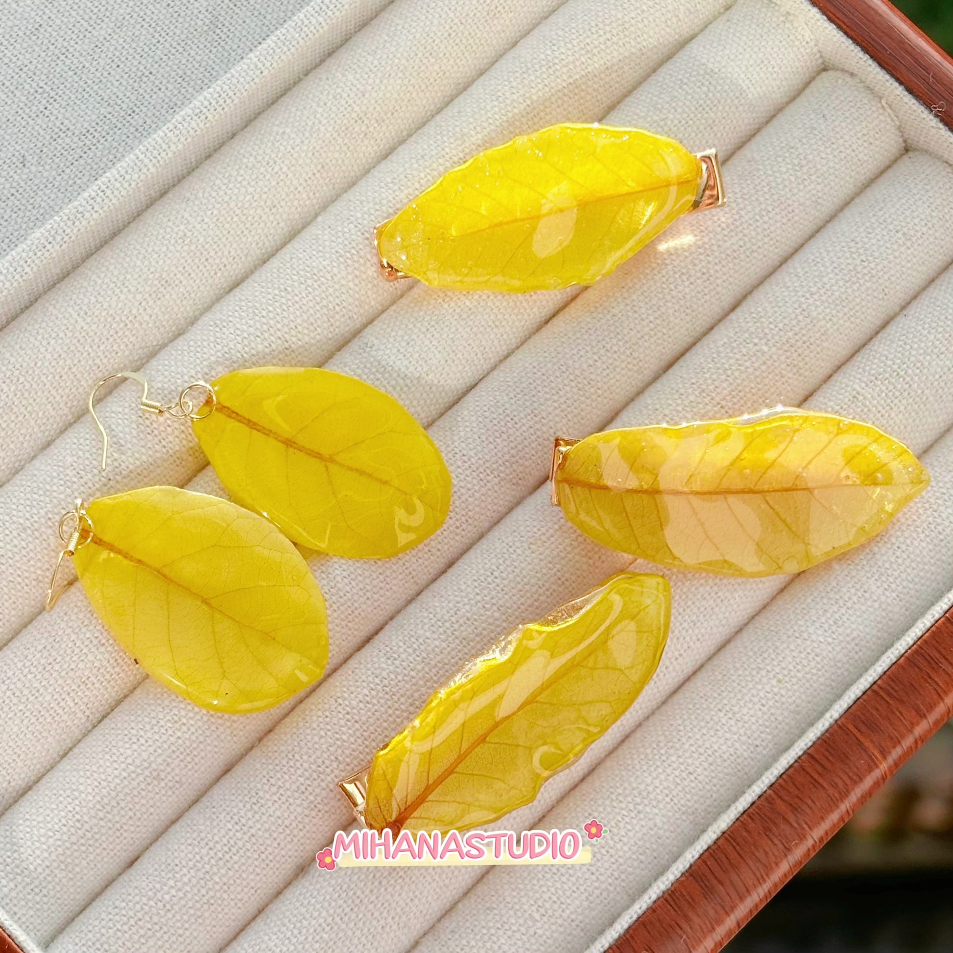 Yellow leaf-shaped earrings on a jewelry display box with 'MIHANA STUDIO' branding.