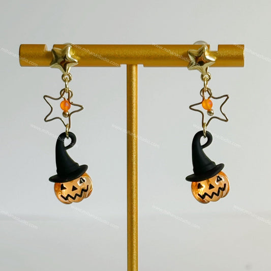 Halloween-themed earrings with jack-o'-lanterns and witch hats on a gold stand.