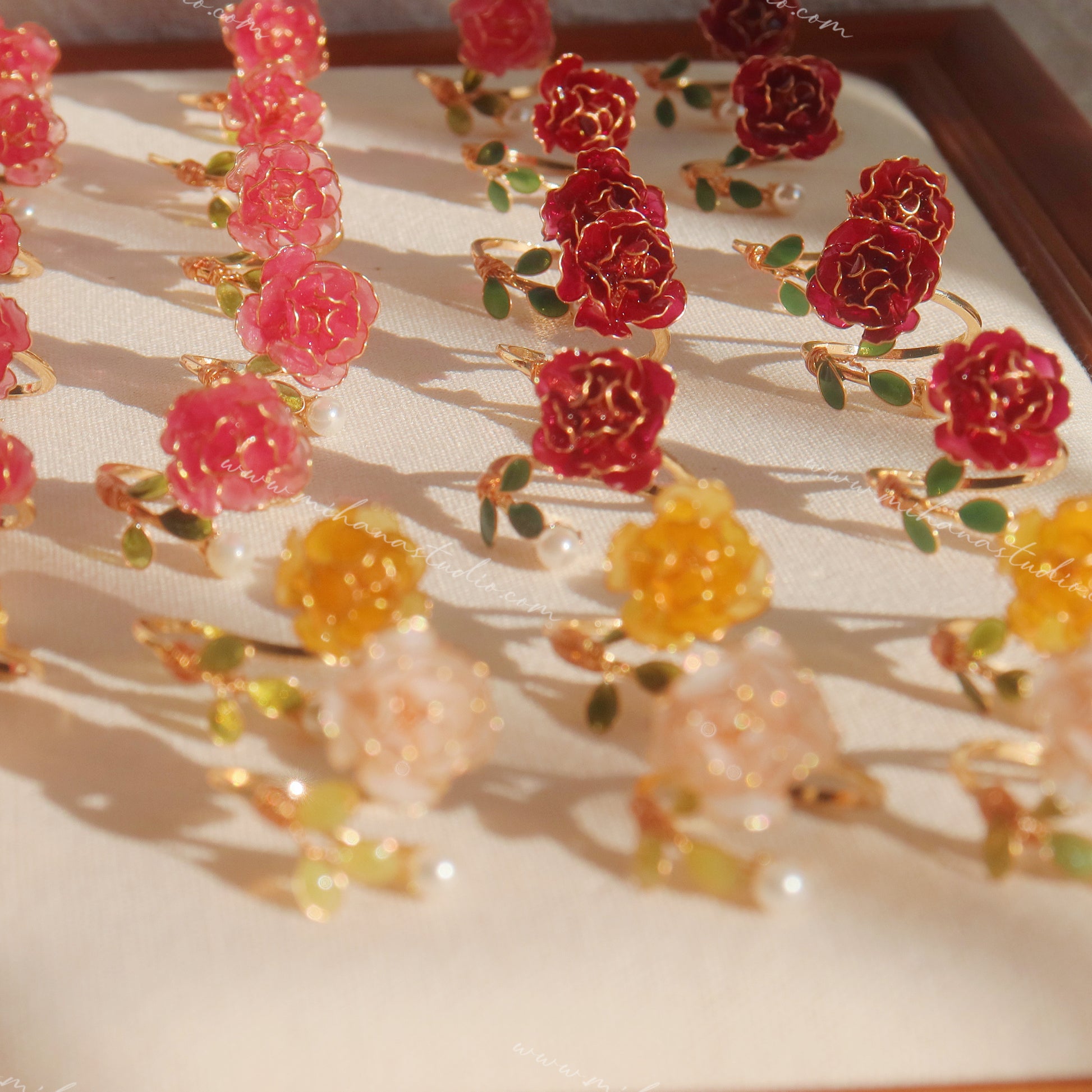 Yellow, white and red rose open rings with green leaves and pearls on a light background.