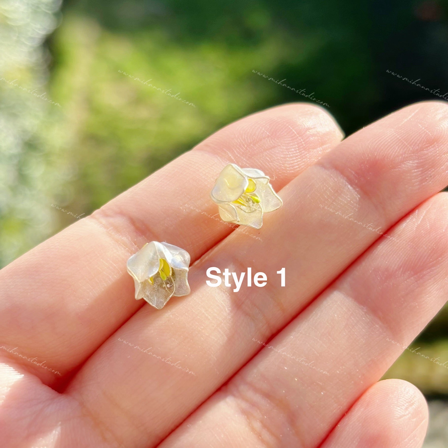 Pair of floral earrings held between fingers with a blurred green background