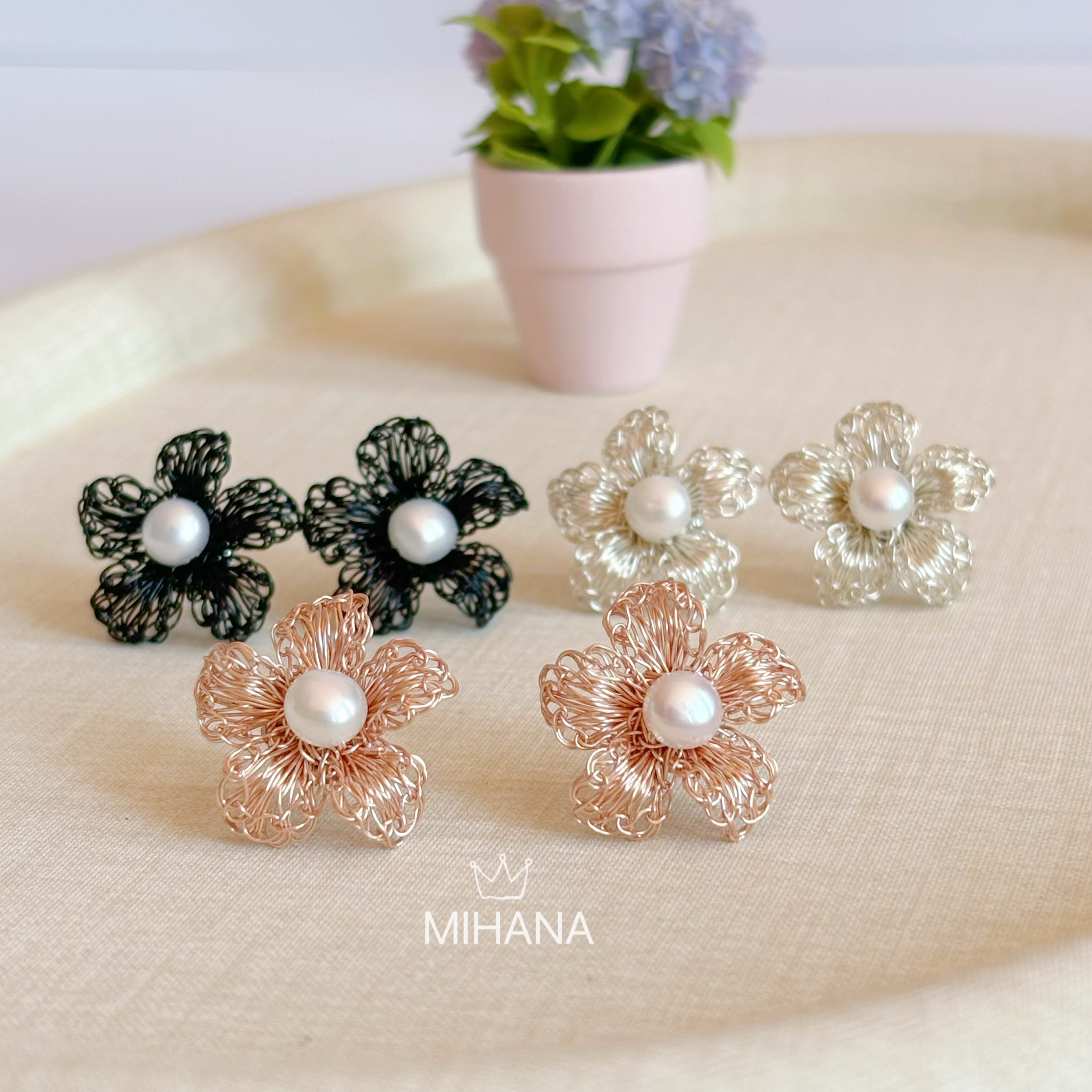 Floral earrings with pearl centers on a beige surface, with 'MIHANA' branding.