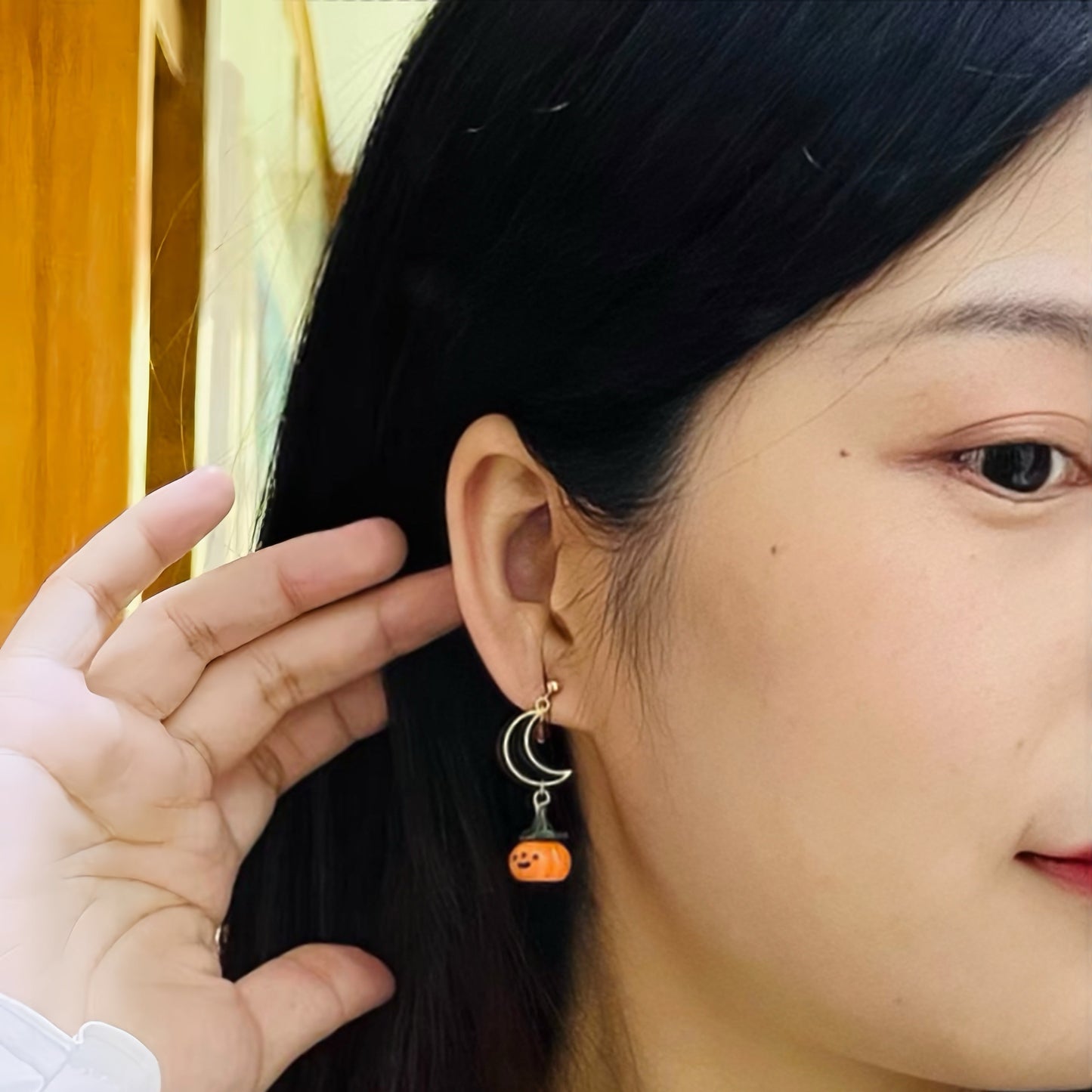 Close-up of a person wearing an earring with a crescent moon and orange gemstone design.