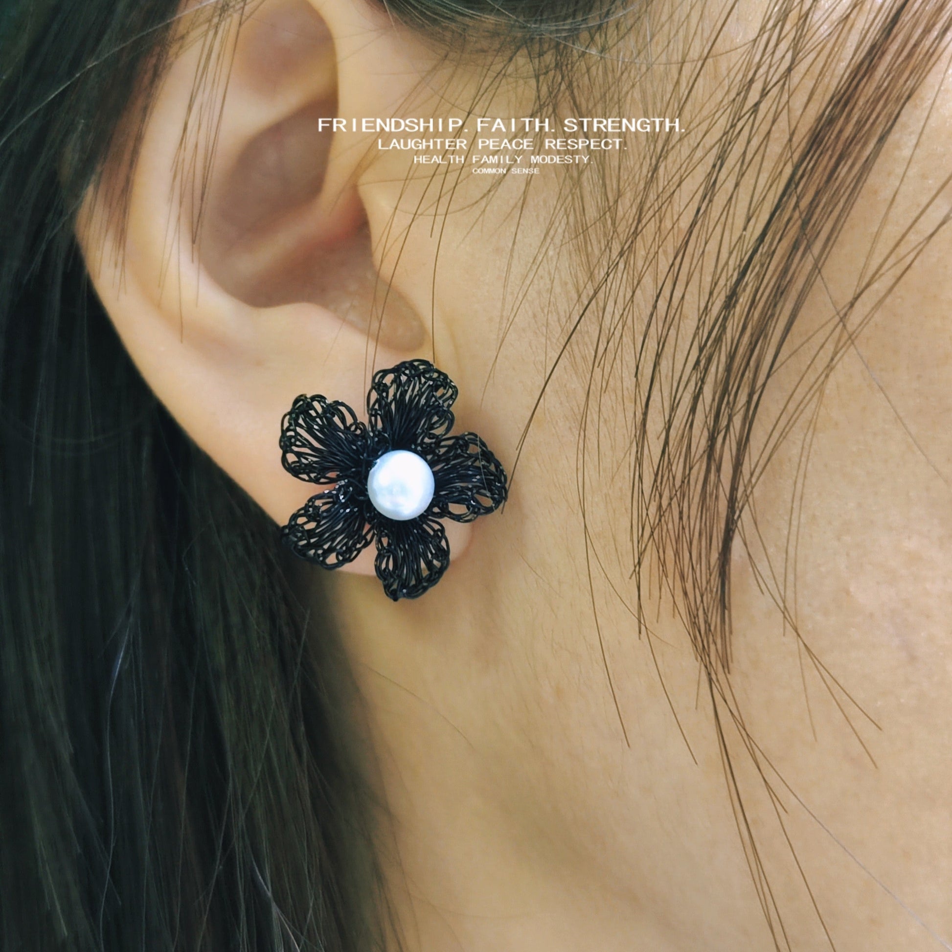Black flower-shaped earring with pearl center worn by a person