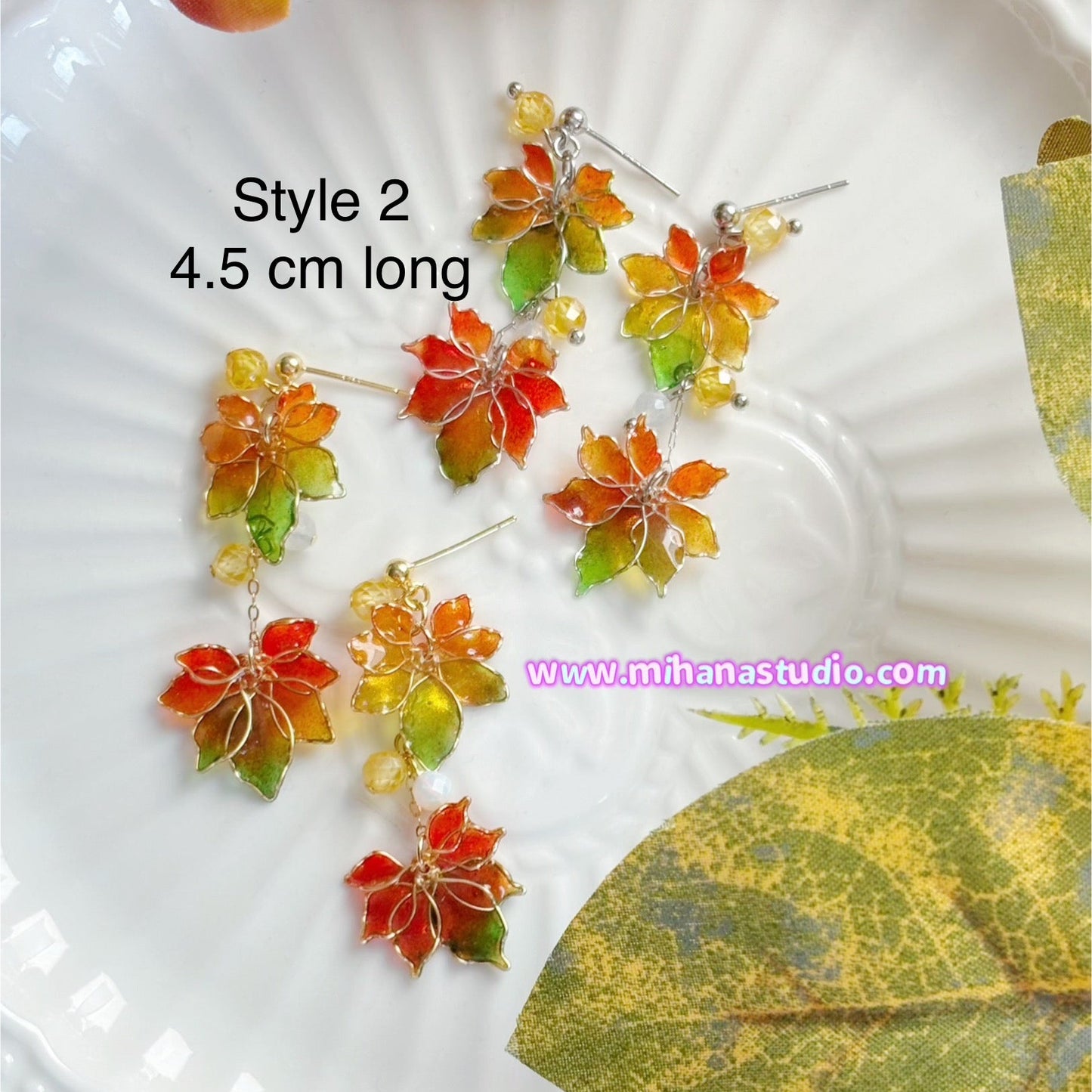 Colourful autumn leaf maple earrings on display in a jewellery box with 'www.mihanastudio.com' branding.