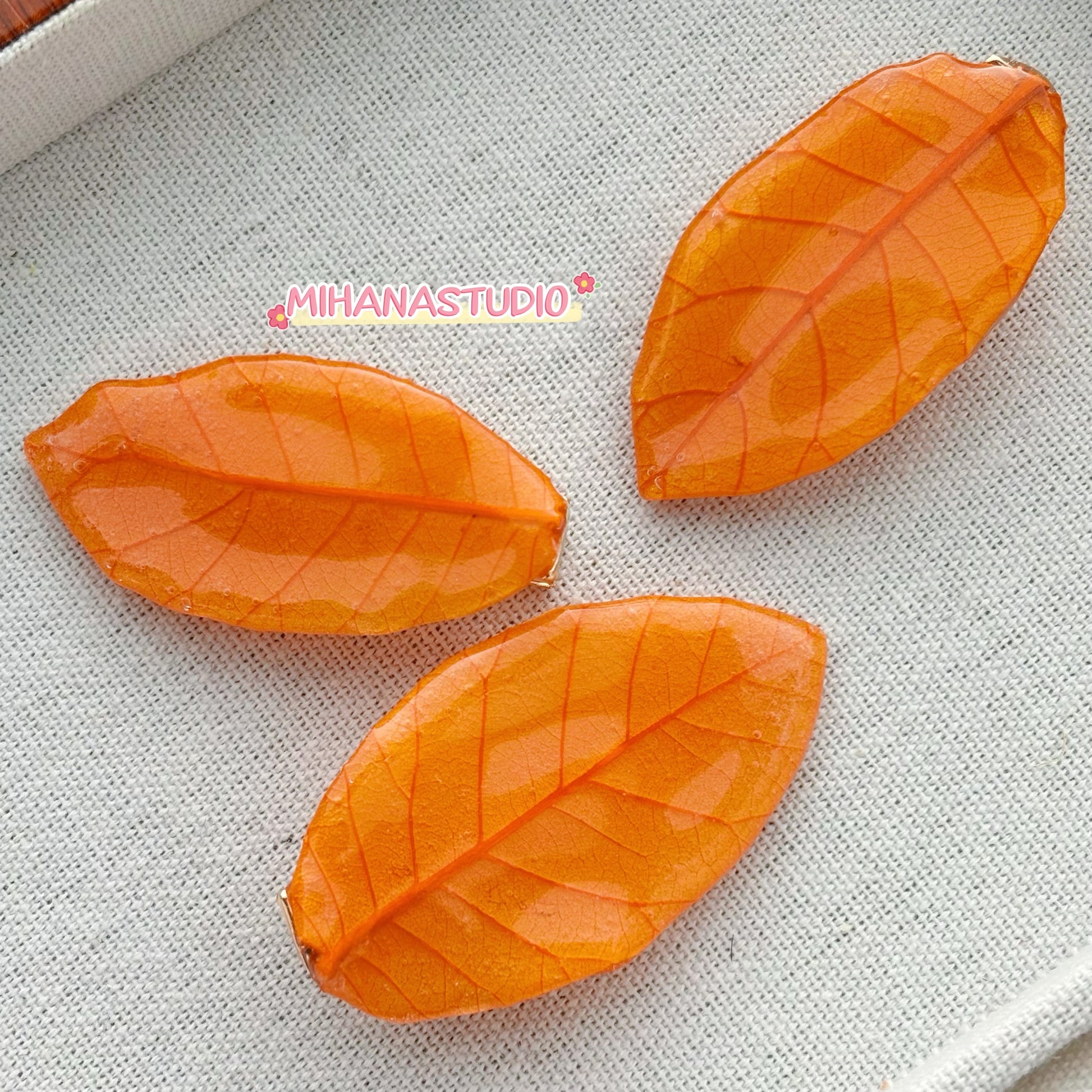 Three orange leaf-shaped objects on a textured gray surface with 'MIHANASTUDIO' branding.