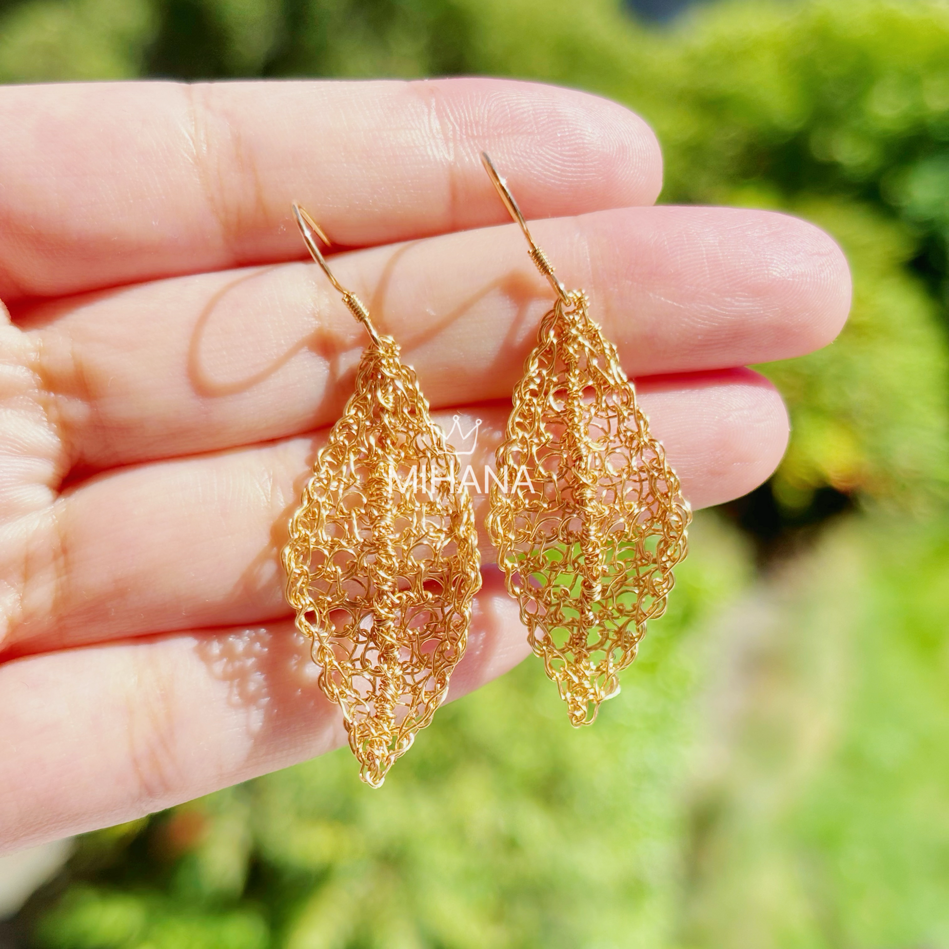 Gold lace earrings held in a hand with a blurred green background