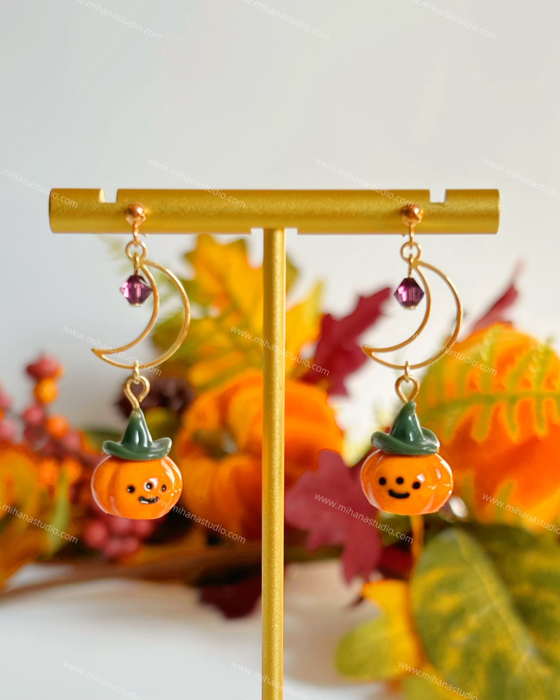 Pumpkin-shaped earrings on a gold stand with a colorful leaf background