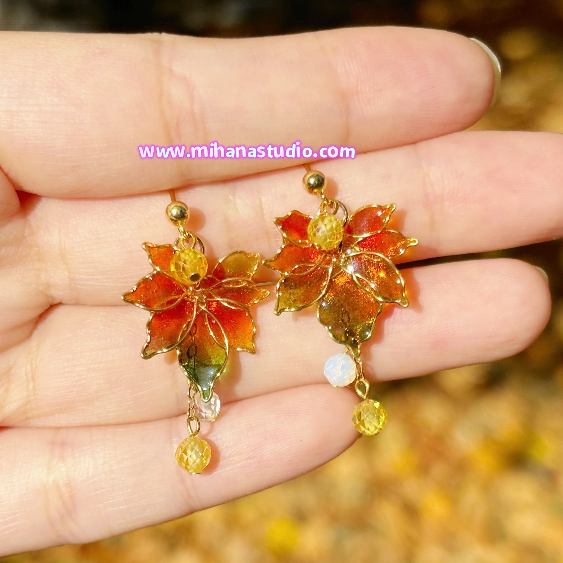 Colorful autumn maple leaf earrings held in a hand with a blurred natural background