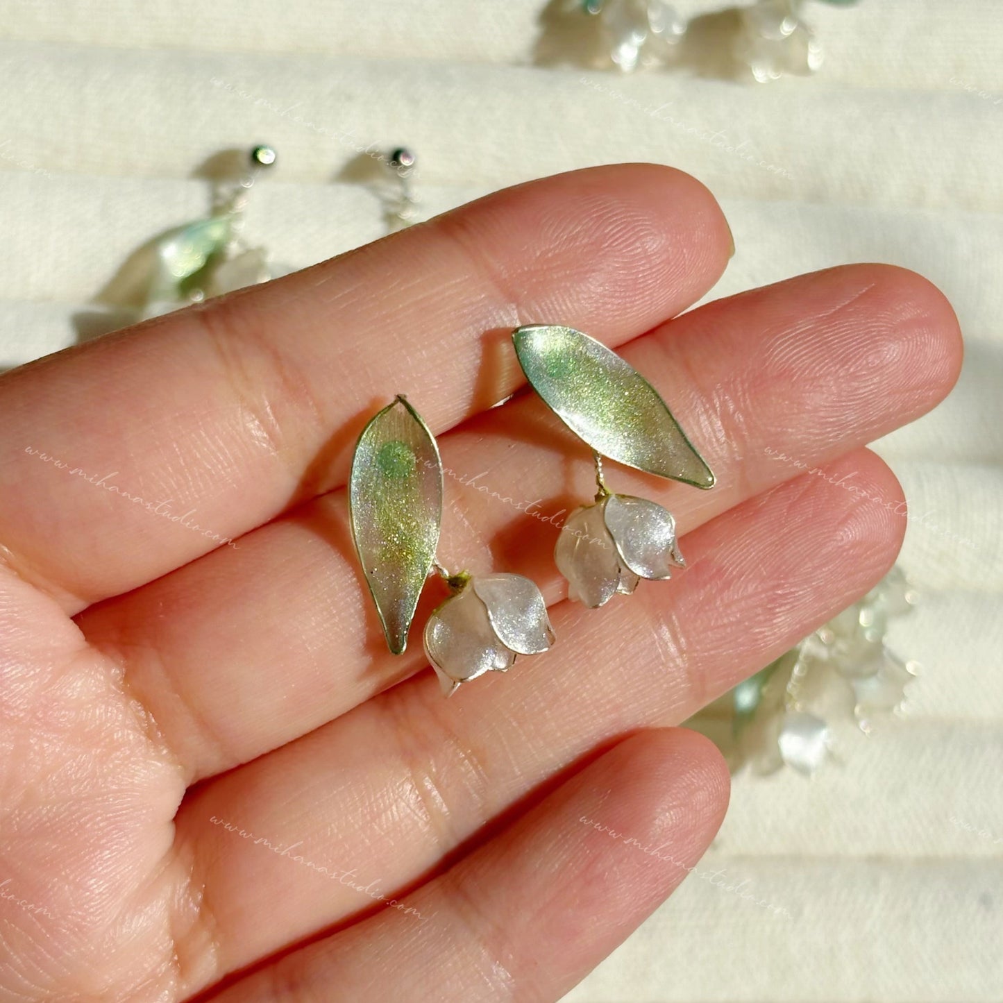 Gold and silver leaf-shaped lily of the valley earrings held between fingers with a blurred background