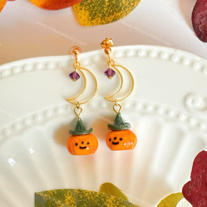 Pumpkin-shaped earrings on a decorative plate with autumn leaves.