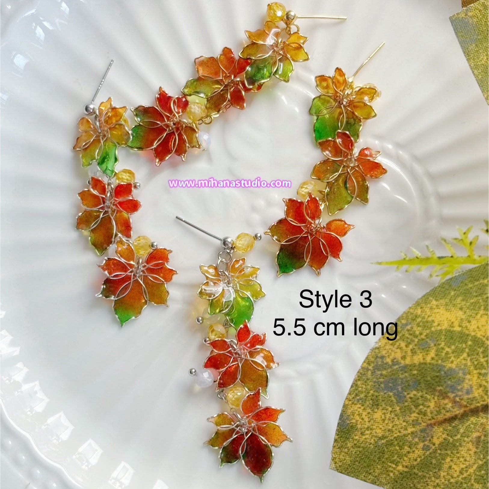 Colourful autumn leaf maple earrings on display in a jewellery box with 'www.mihanastudio.com' branding.