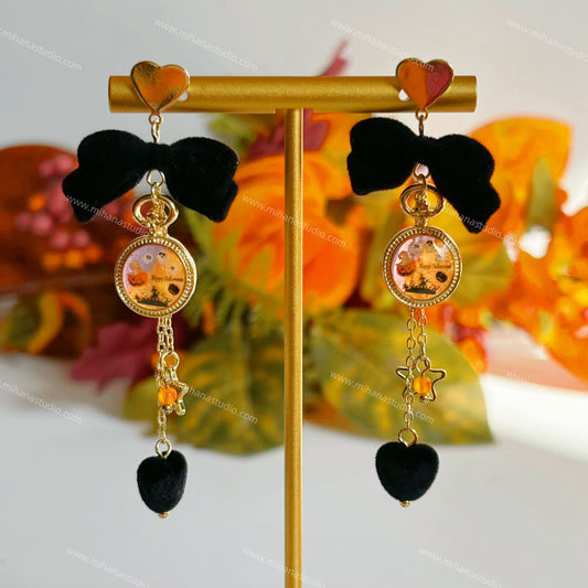 Black bow earrings with heart and star charms on a gold stand against a floral background