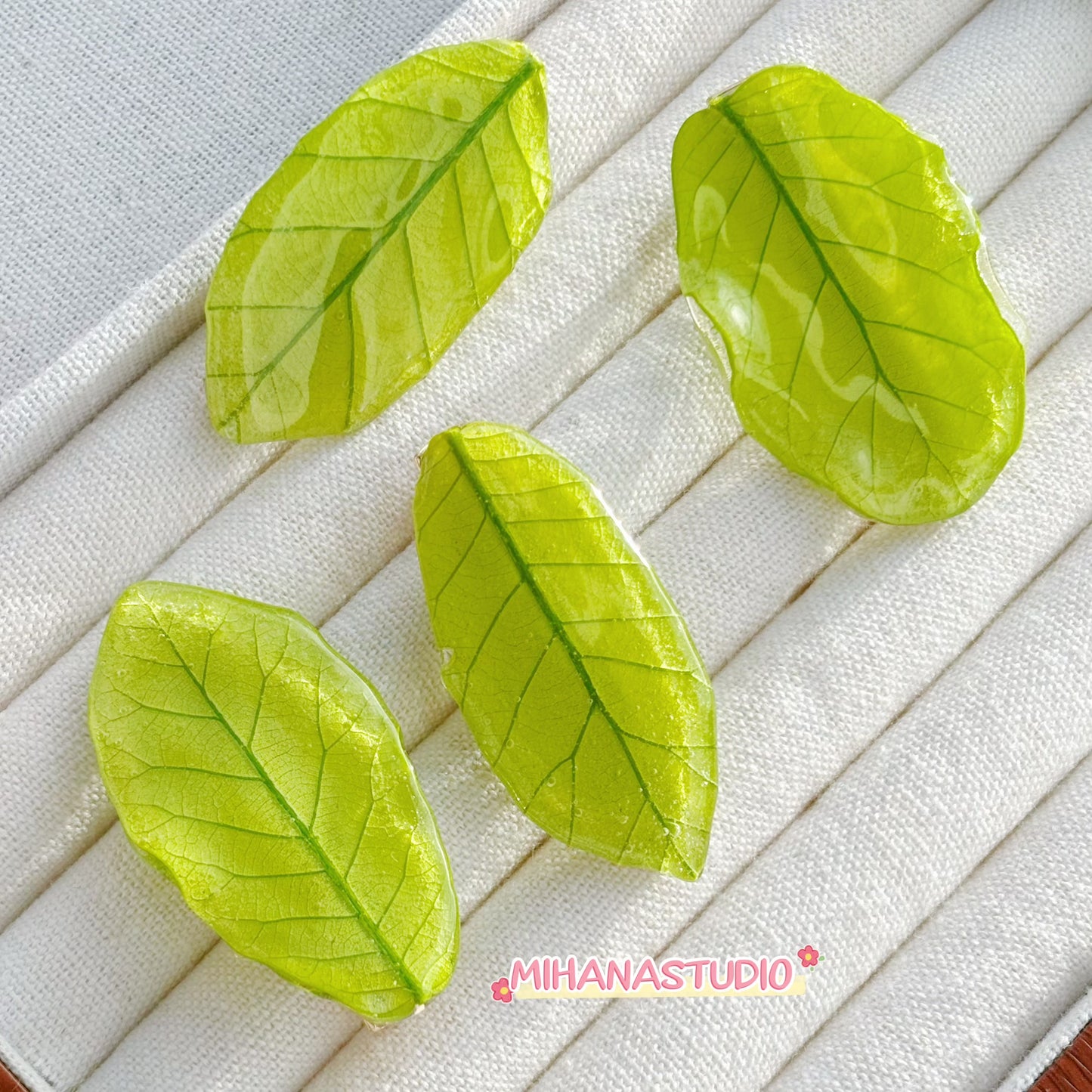 Four green leaf-shaped objects on a textured white surface with 'MIHANASTUDIO' branding.