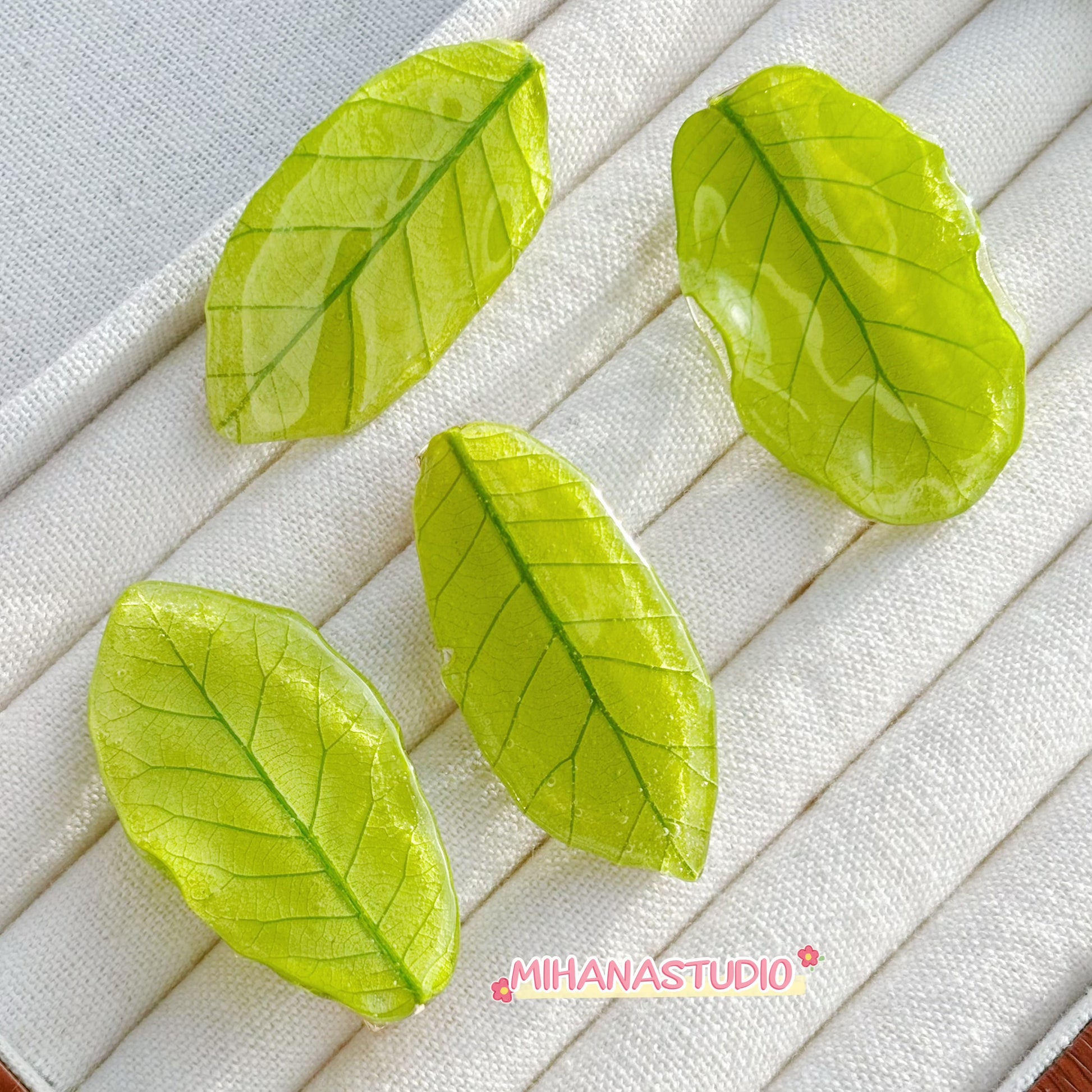 Four green leaf-shaped objects on a textured white surface with 'MIHANASTUDIO' branding.