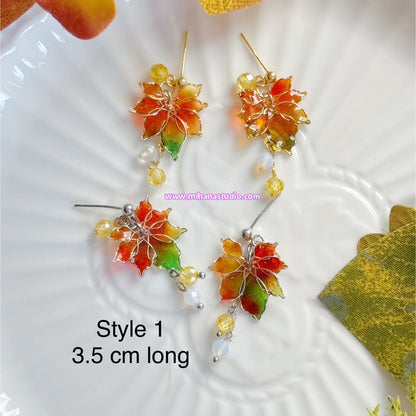 Colourful autumn leaf maple earrings on display in a jewellery box with 'www.mihanastudio.com' branding.