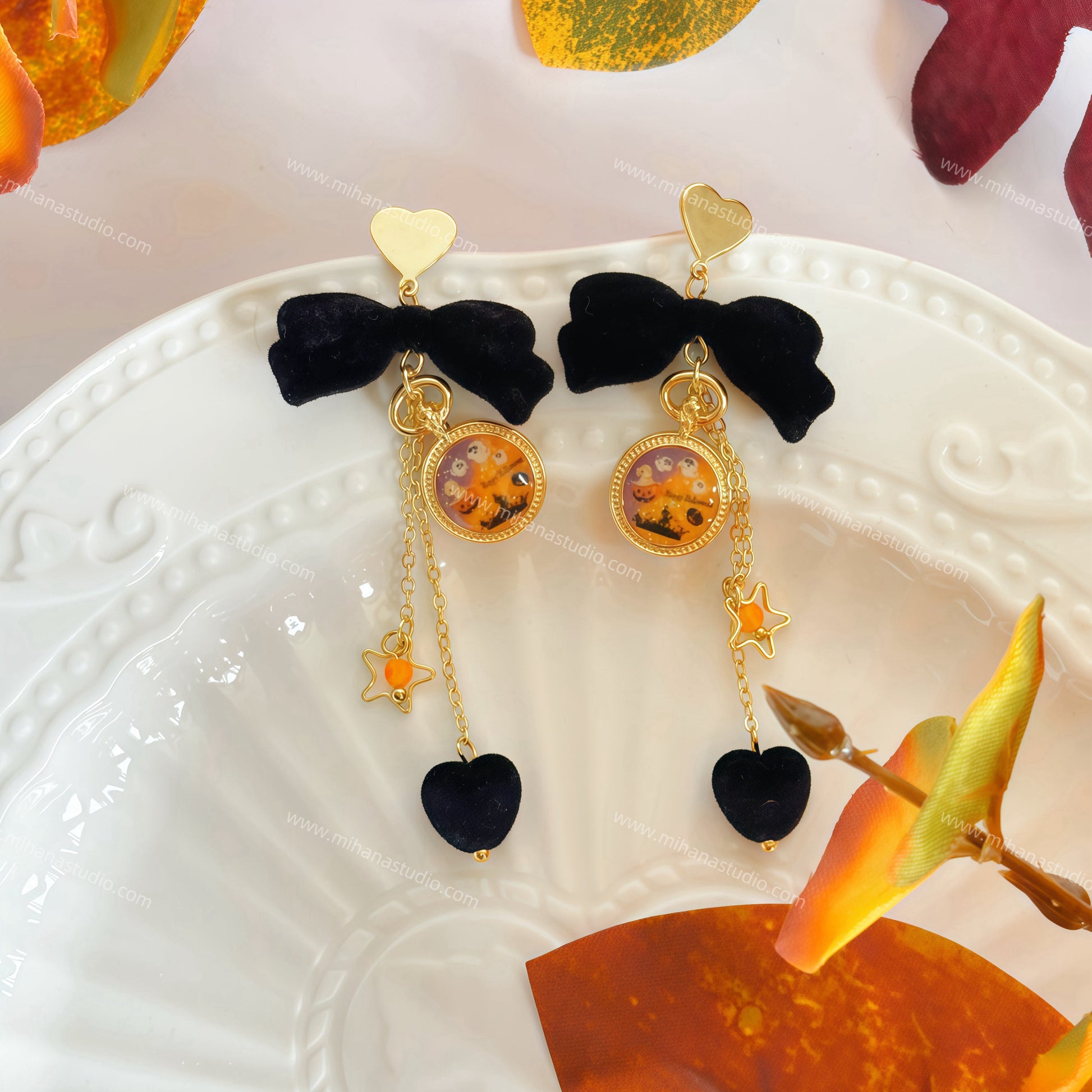 Pair of earrings with black bows and colorful charms on a decorative plate with autumn leaves.