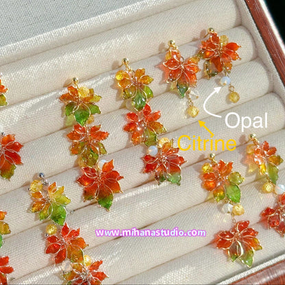 Colourful autumn leaf maple earrings on display in a jewellery box with 'www.mihanastudio.com' branding.