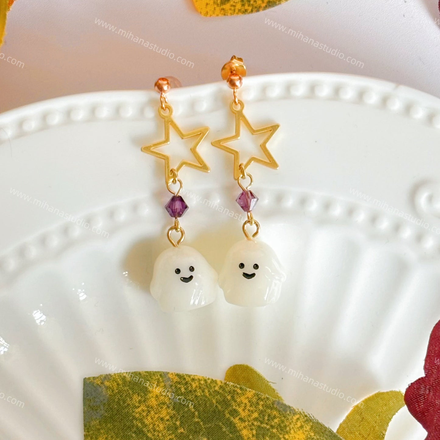 Ghost-shaped earrings with star details on a decorative plate with autumn leaves.