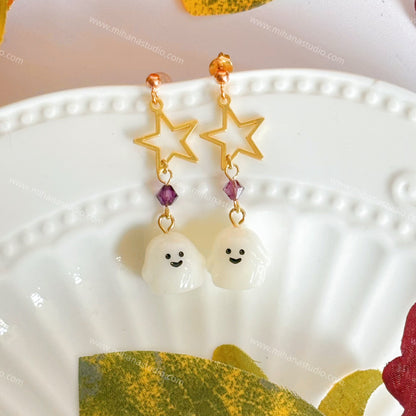 Ghost-shaped earrings with star details on a decorative plate with autumn leaves.