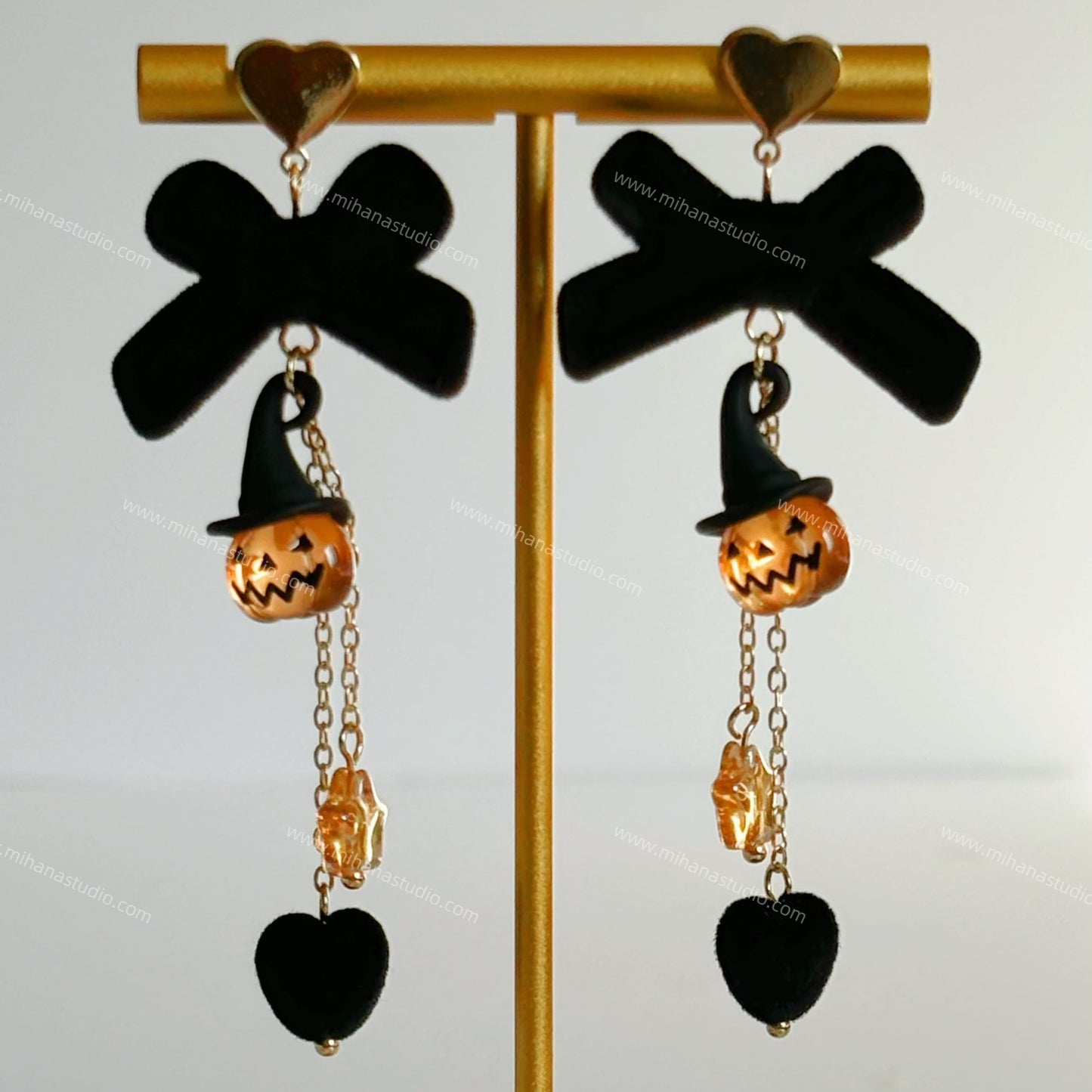 Halloween-themed earrings with jack-o'-lanterns and black bows on a gold stand.
