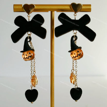 Halloween-themed earrings with jack-o'-lanterns and black bows on a gold stand.