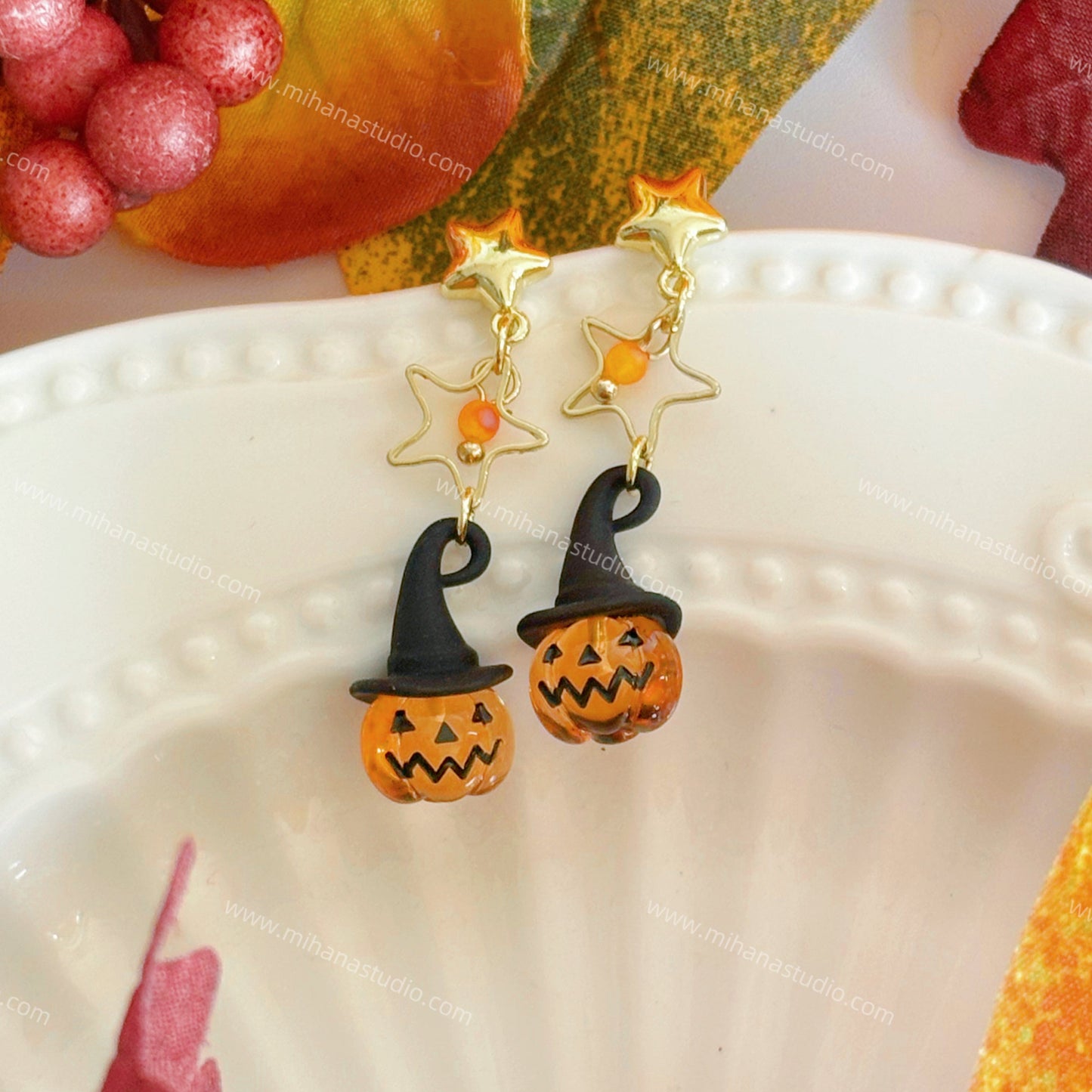 Pumpkin earrings on a white plate with autumn decorations.