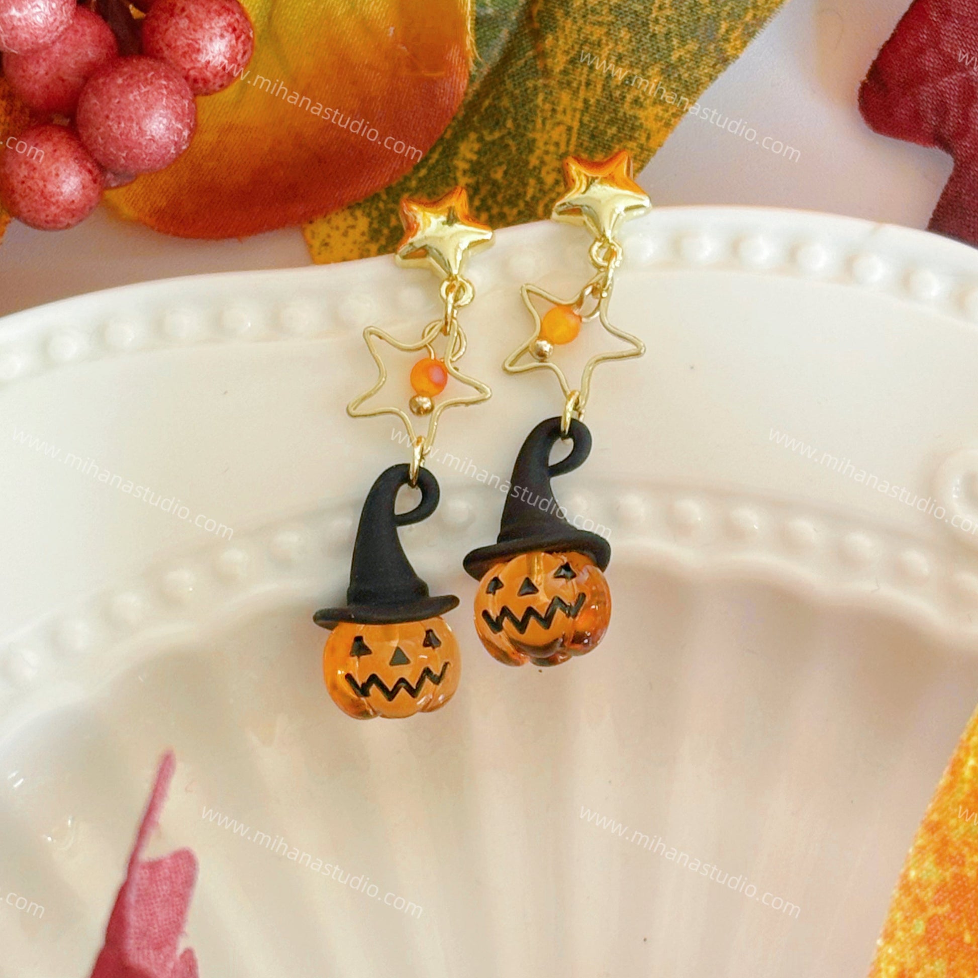 Pumpkin earrings on a white plate with autumn decorations.