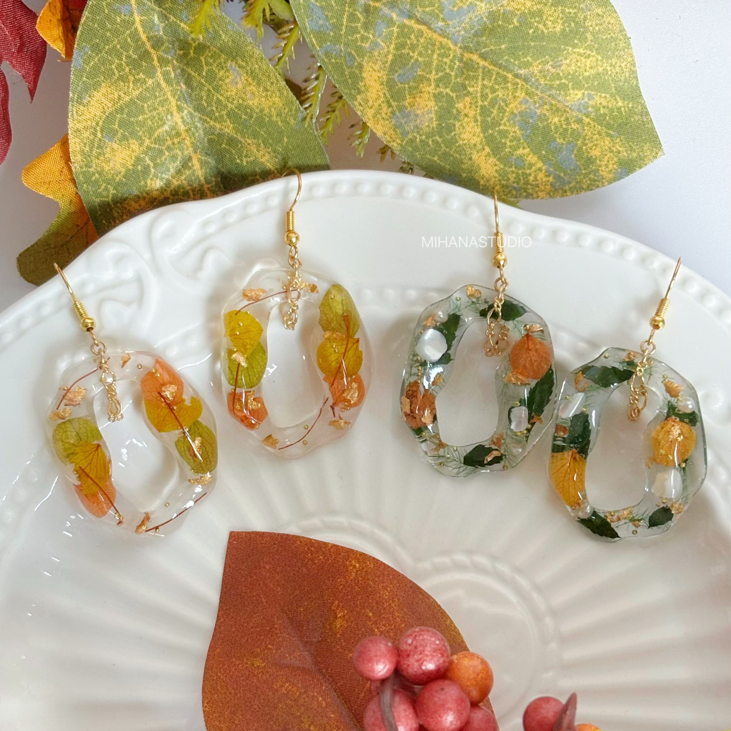 Pair of earrings with autumn-themed design on a decorative plate with leaves and berries.