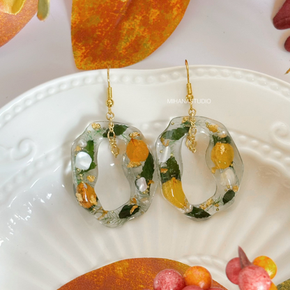 Hoop earrings with floral and fruit design on a white plate with autumn leaves.
