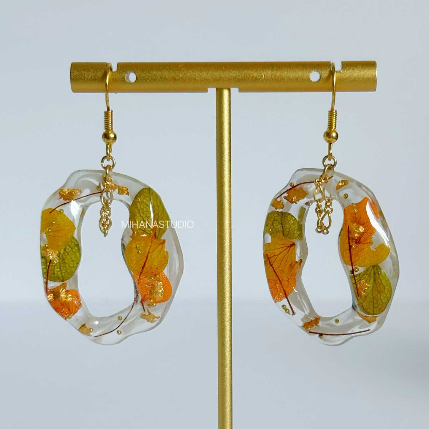 Earrings with floral design in clear resin on a gold stand against a light gray background