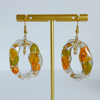 Earrings with floral design in clear resin on a gold stand against a light gray background