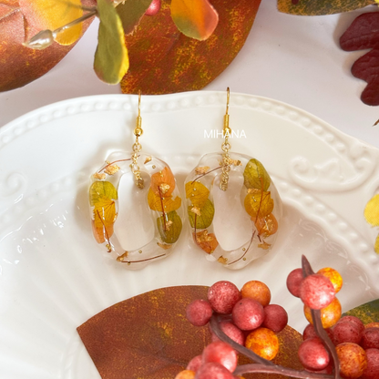 Pair of earrings with colorful beads on a white dish with autumn leaves and berries.